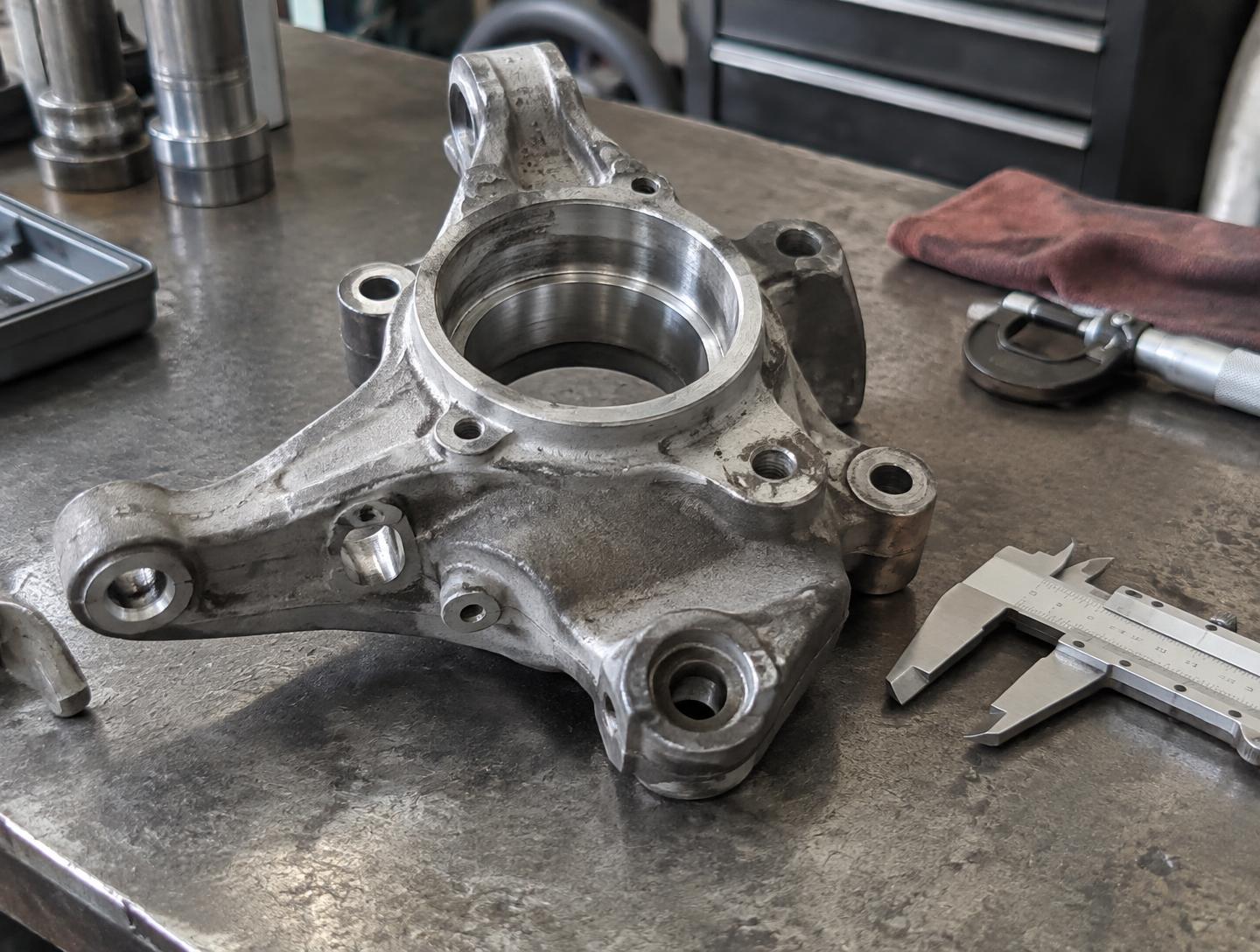Machined automotive component on a workbench beside inspection calipers